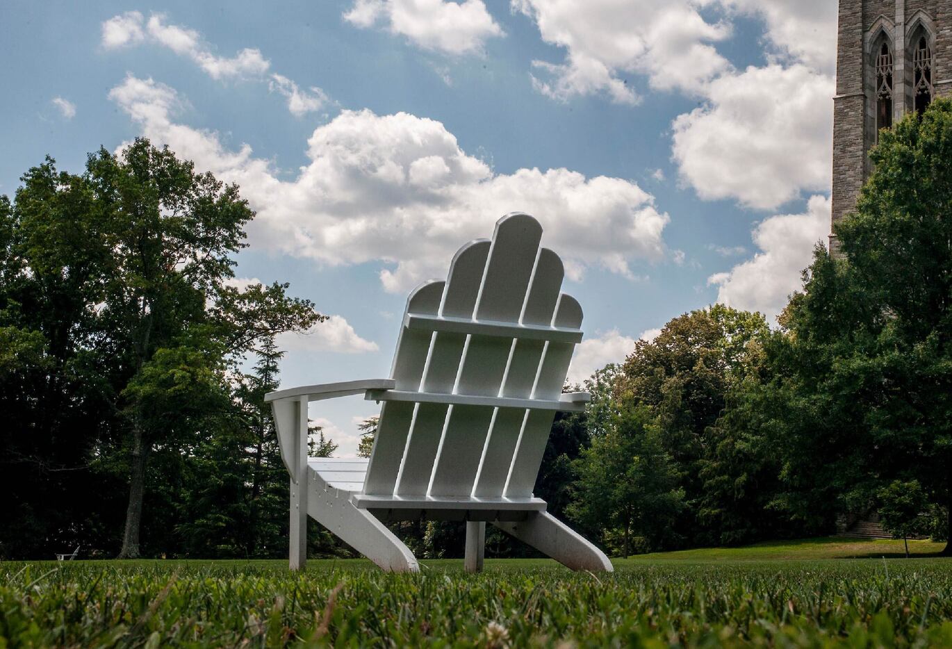an image of a white Adirondack chair on a lawn with a blue sky and puffy clouds